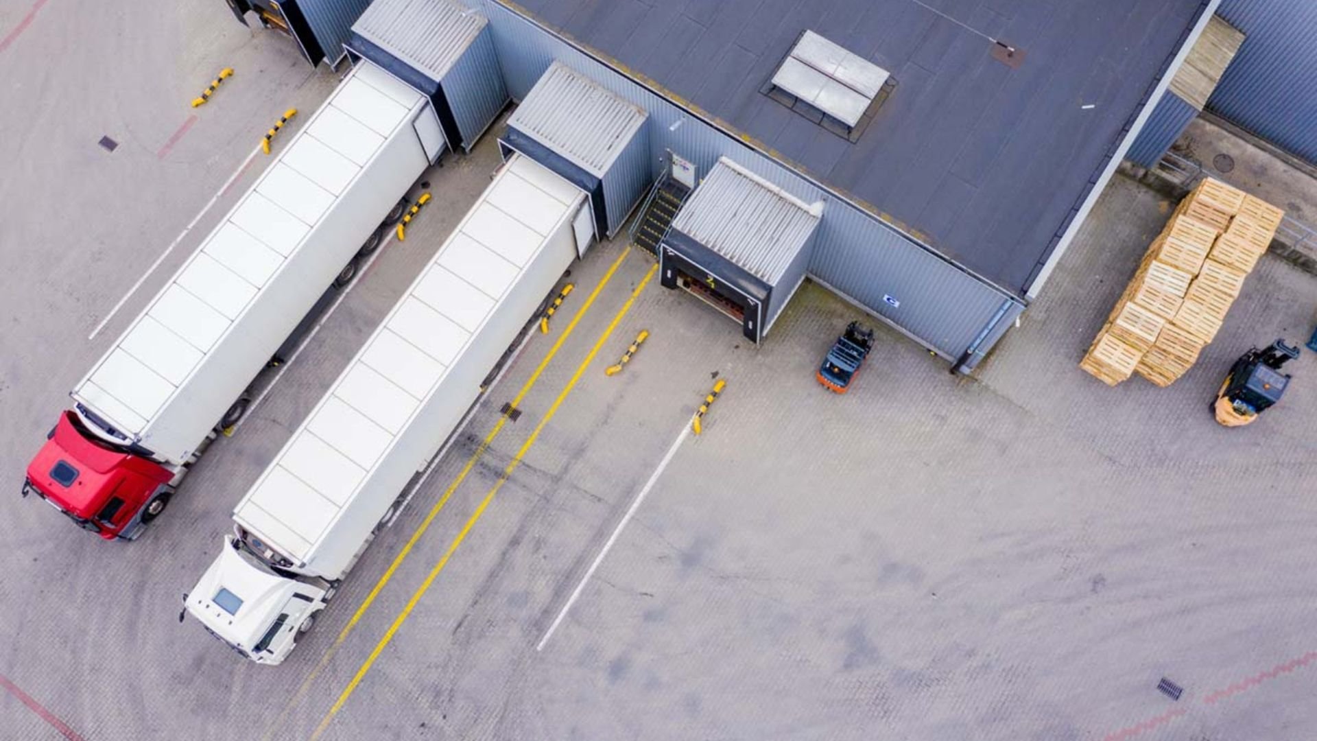 Aerial view of warehouse loading dock with trucks, forklifts, and wooden pallets