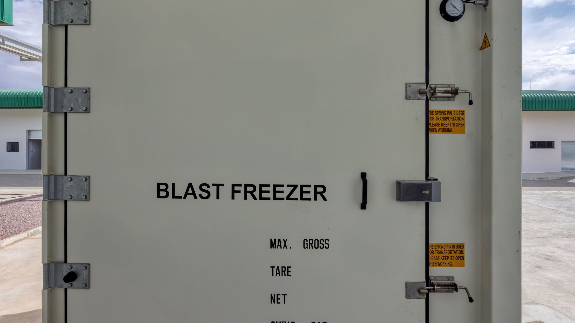Industrial blast freezer door with metal hinges and warning labels