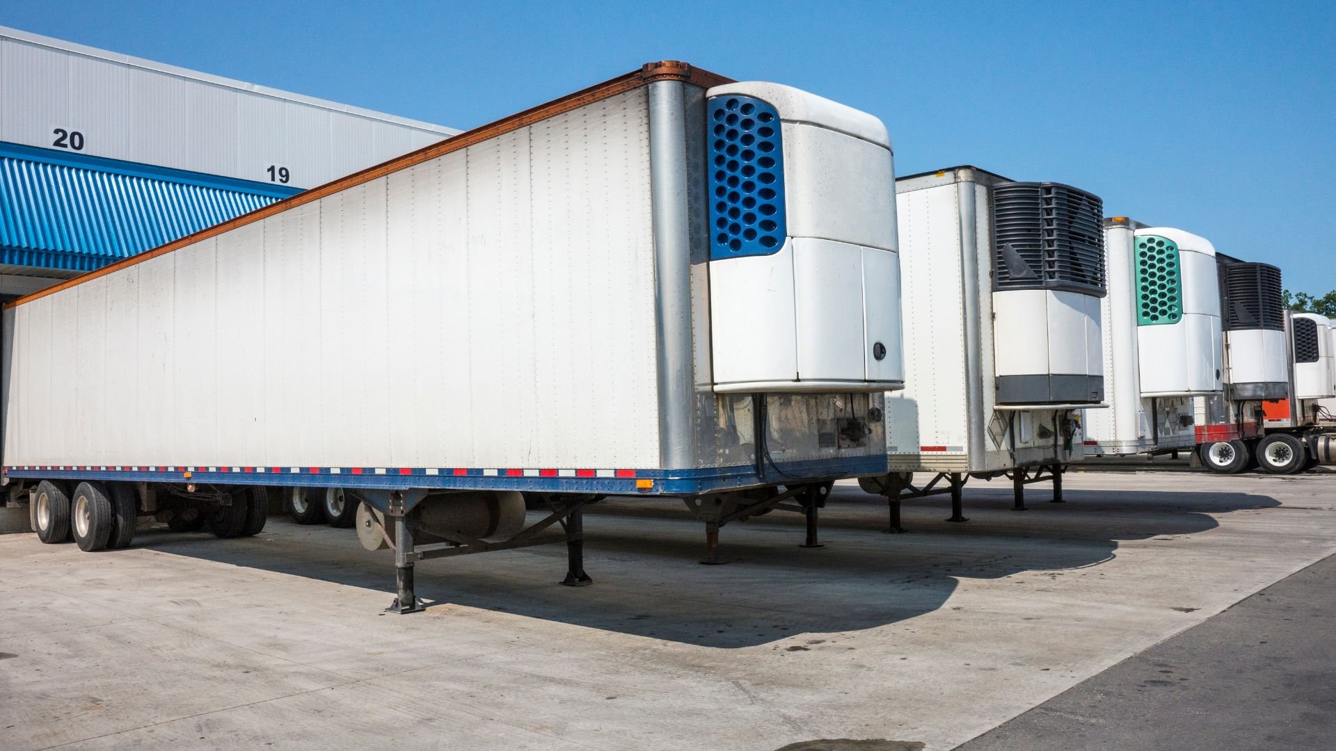 White refrigerated semi-trailers with cooling units parked in industrial lot