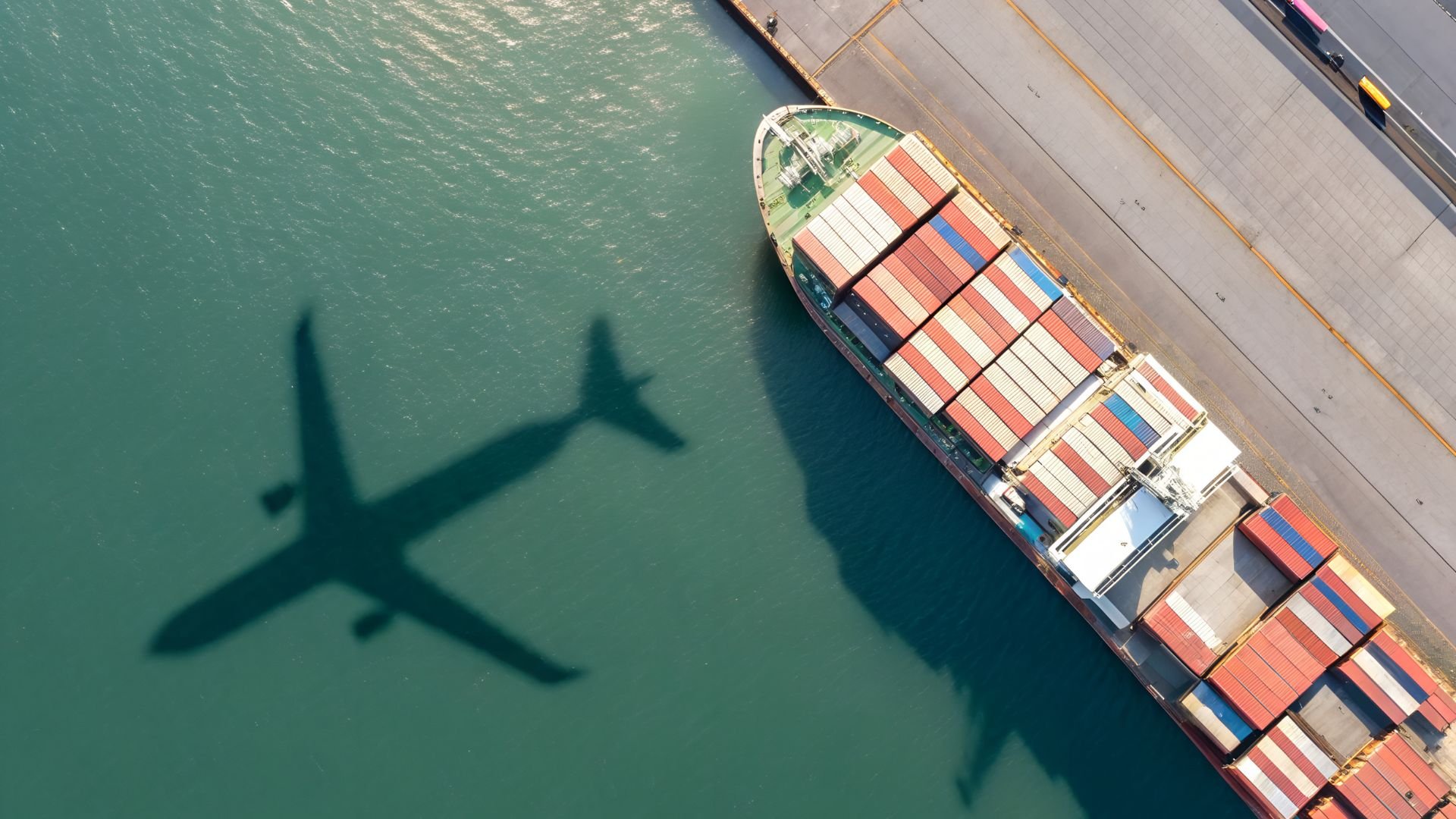 Cargo ship and airplane shadow on turquoise water at port