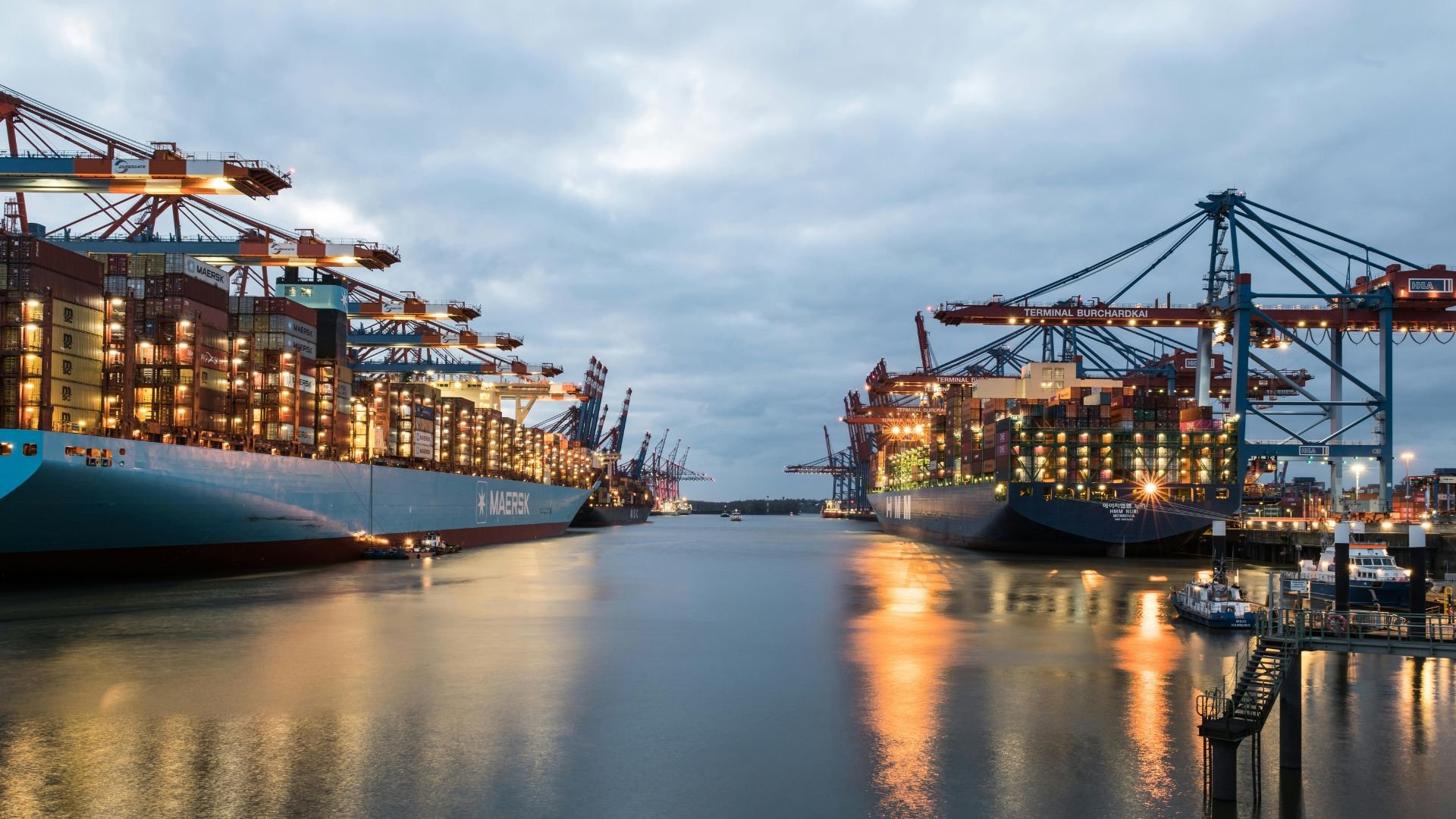 Maersk container ships docked at illuminated port terminal at dusk