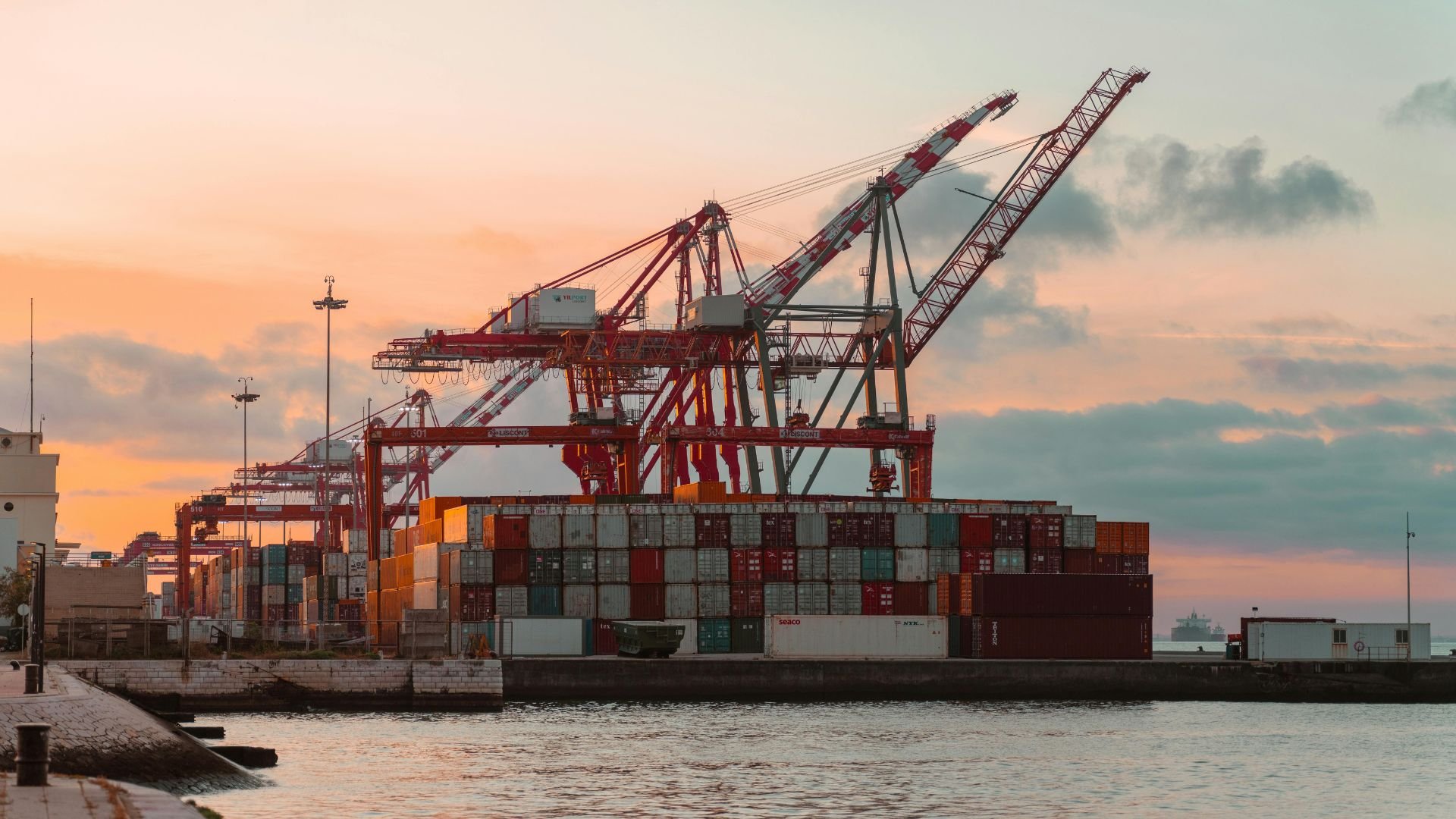 Cargo cranes and shipping containers at industrial port during sunset