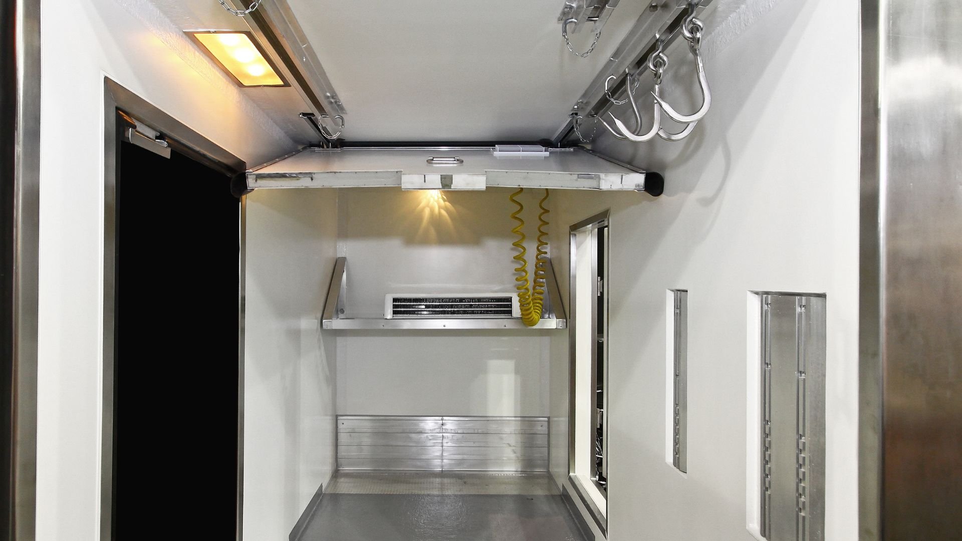 Industrial refrigeration unit interior with shelves and yellow coiled hoses